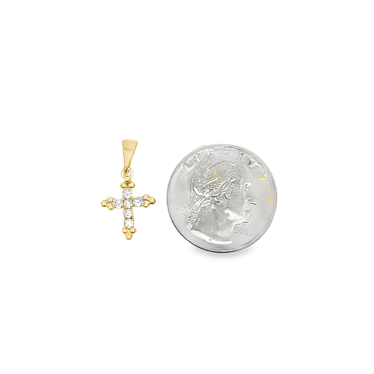 A small gold cross pendant adorned with sparkling diamonds sits next to a US quarter for size comparison.
