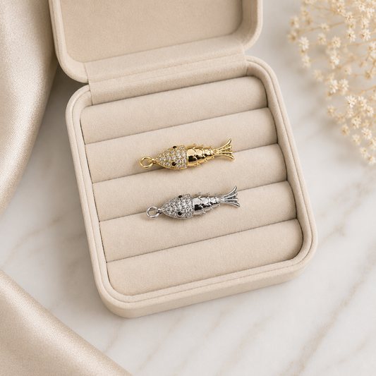 A gold and silver pave-set crystal fish pendant rests inside a beige velvet jewelry box.