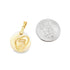 A round gold pendant featuring a mother and child inside a heart rests next to a US quarter coin for scale.