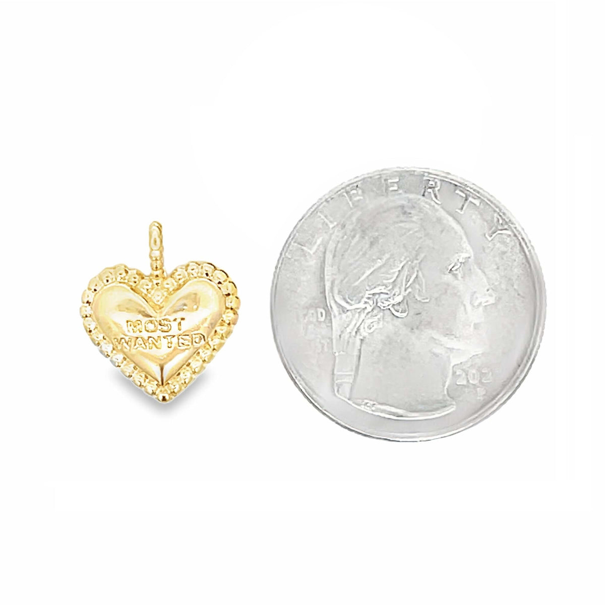 A small gold heart-shaped charm with the words "MOST WANTED" engraved on its surface rests next to a US quarter for scale.
