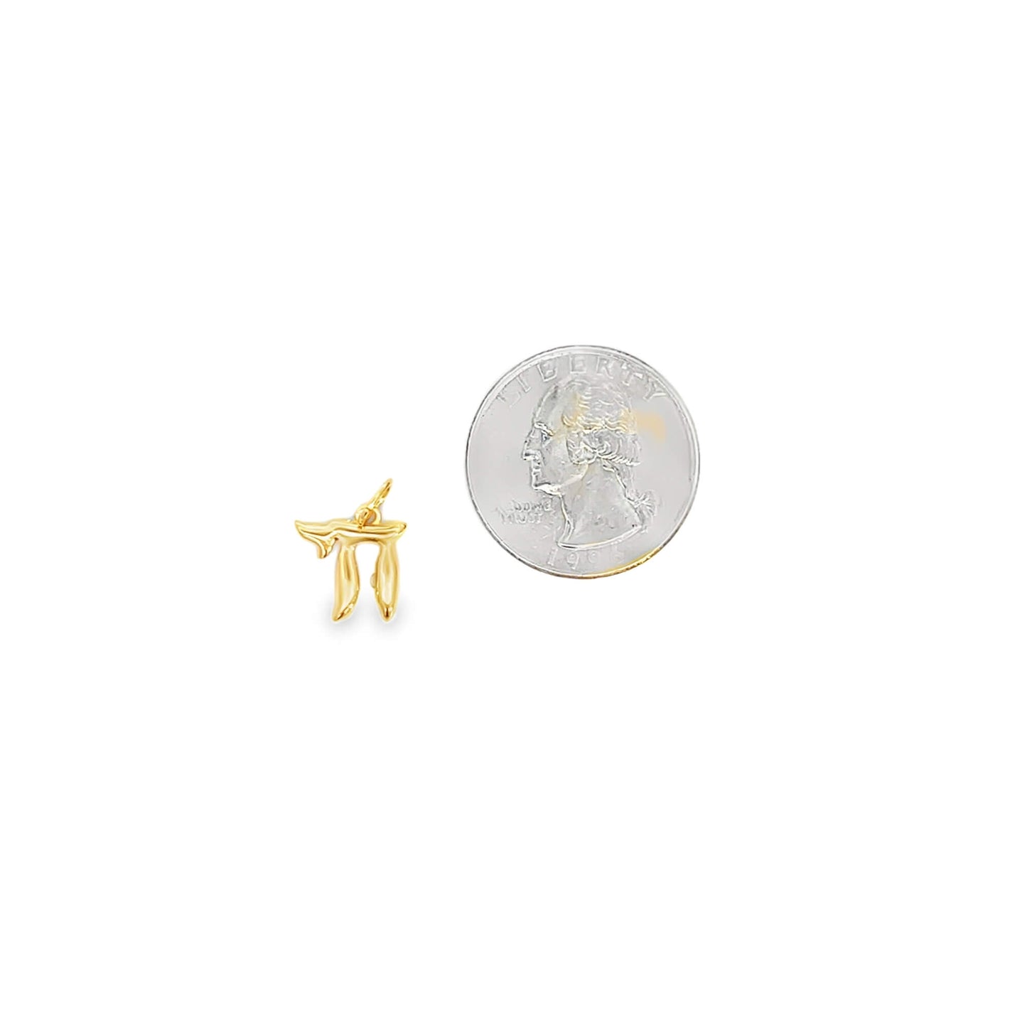 A small gold Chai pendant rests next to a US quarter coin for scale on a white background.