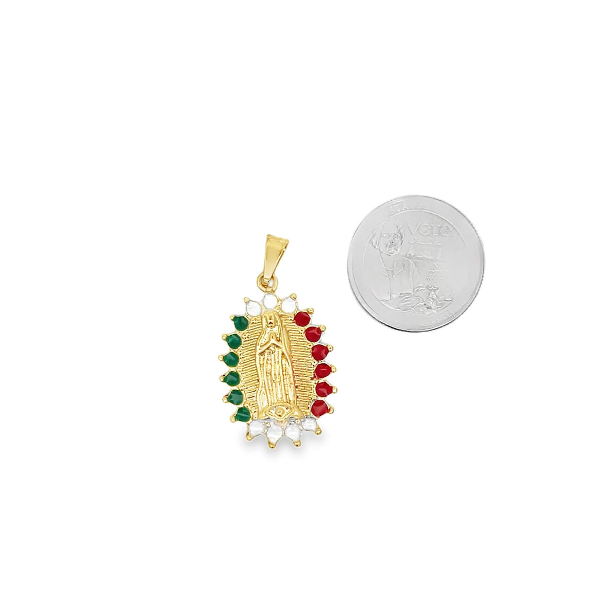 A gold Our Lady of Guadalupe pendant rests next to a coin for scale, showcasing alternating red and green stones framing the central figure.