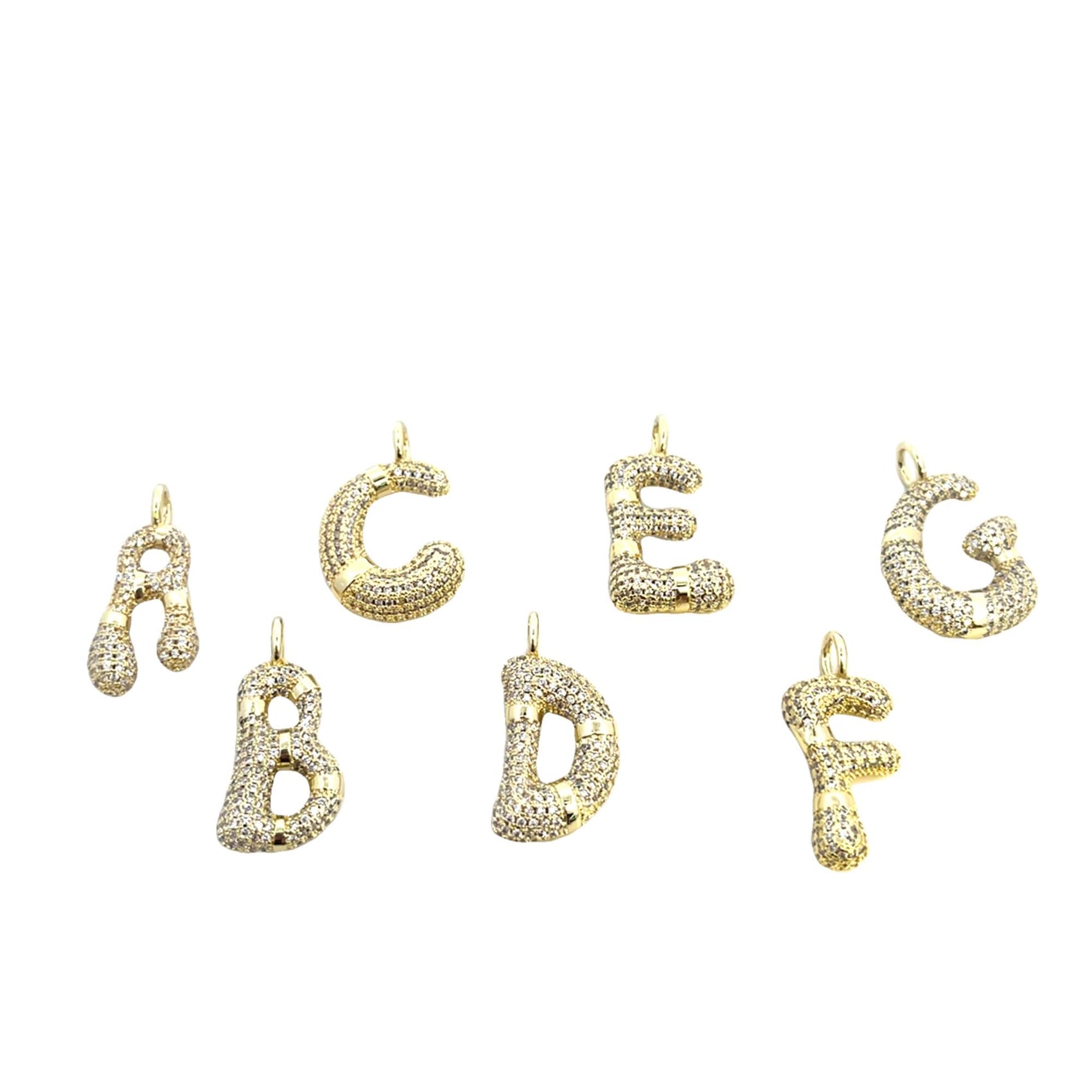 Seven gold alphabet letter charms, from A to G, encrusted with sparkling pave diamonds rest against a plain white background.