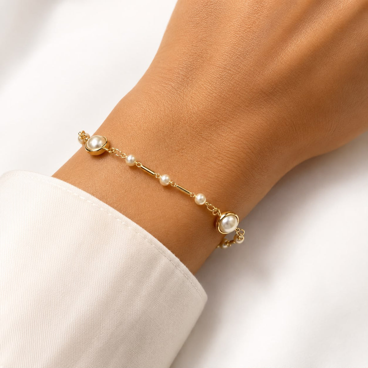 A person wears an elegant gold chain bracelet adorned with delicate pearls around their wrist.