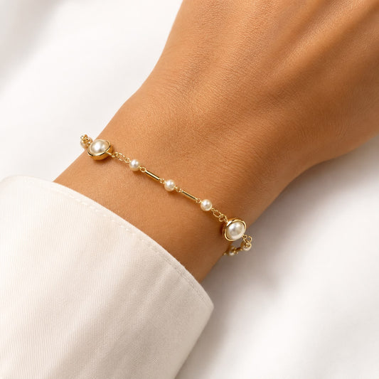 A person wears an elegant gold chain bracelet adorned with delicate pearls around their wrist.
