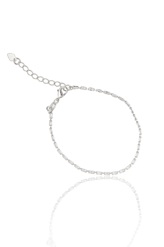 A delicate silver tennis bracelet encrusted with sparkling baguette-cut zirconia stones rests on a reflective white surface, showcasing its adjustable chain and lobster clasp.