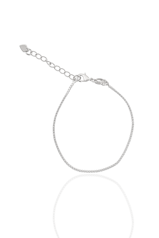 A delicate silver tennis bracelet sparkles against a white background, featuring a lobster clasp and an adjustable chain with a tiny heart charm.