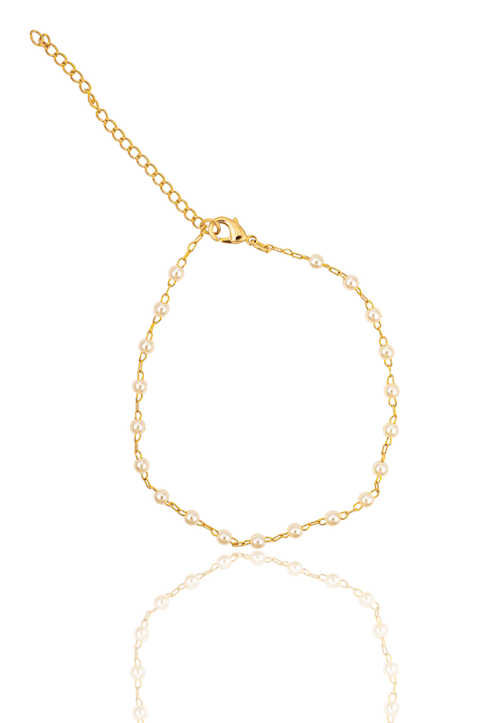 A delicate gold chain bracelet featuring alternating white pearls and a lobster clasp rests against a clean white background, reflecting softly on the surface below.