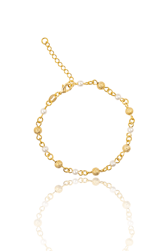 A delicate gold bracelet featuring alternating pearl beads and textured gold balls is displayed on a reflective white surface.