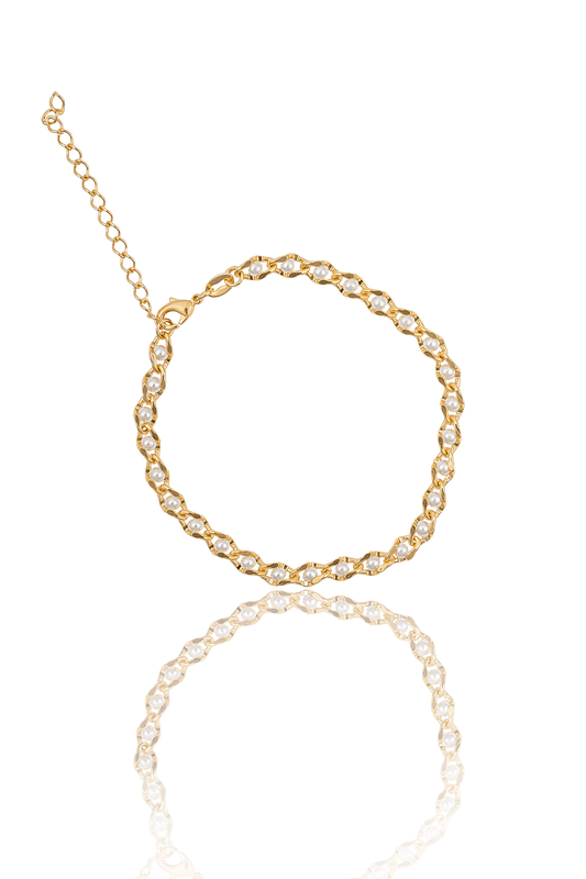 A gold chain bracelet adorned with small pearls lies flat with its reflection on a white surface.