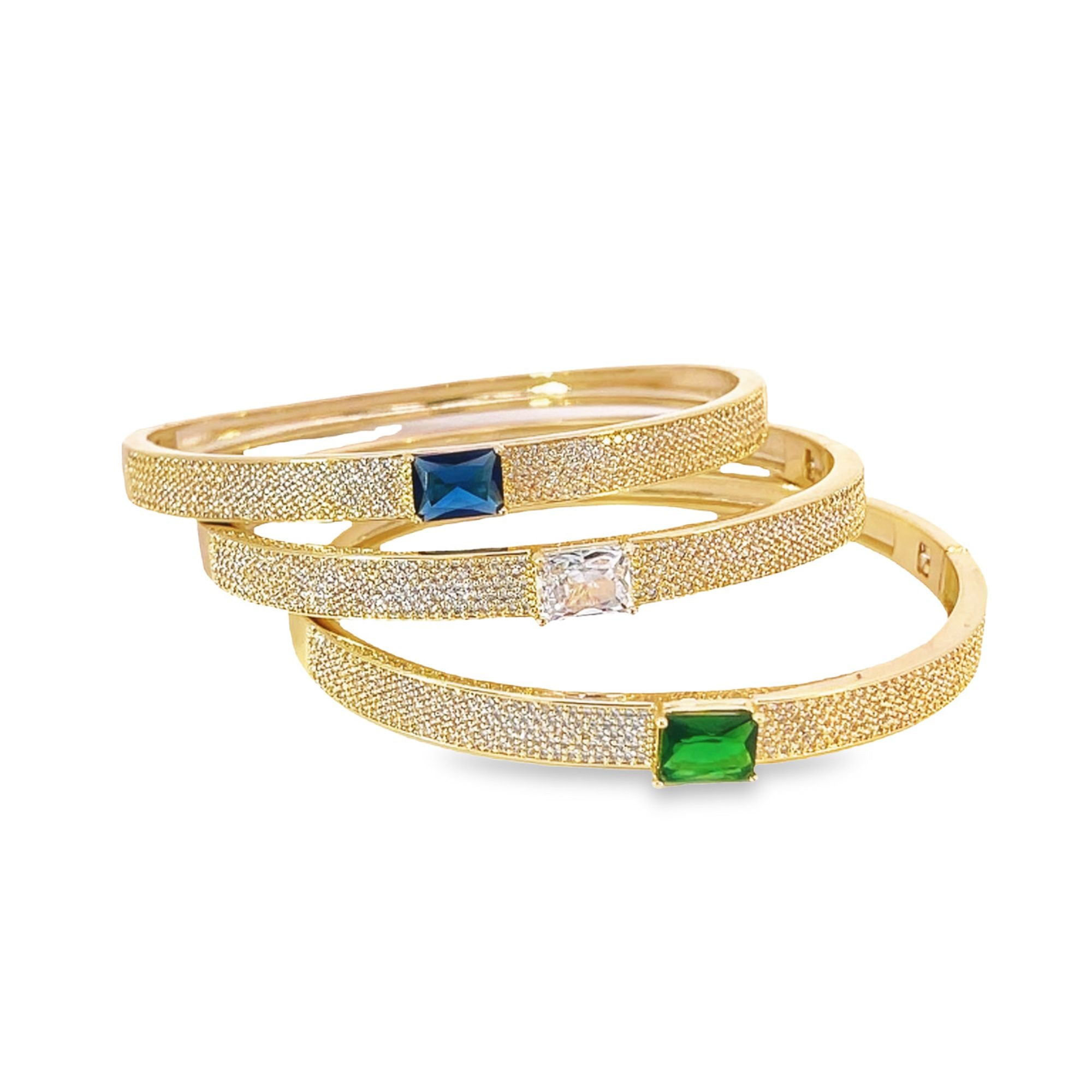 Three sparkling gold pave-set diamond bangles feature a blue sapphire, a clear diamond, and a green emerald gemstone.