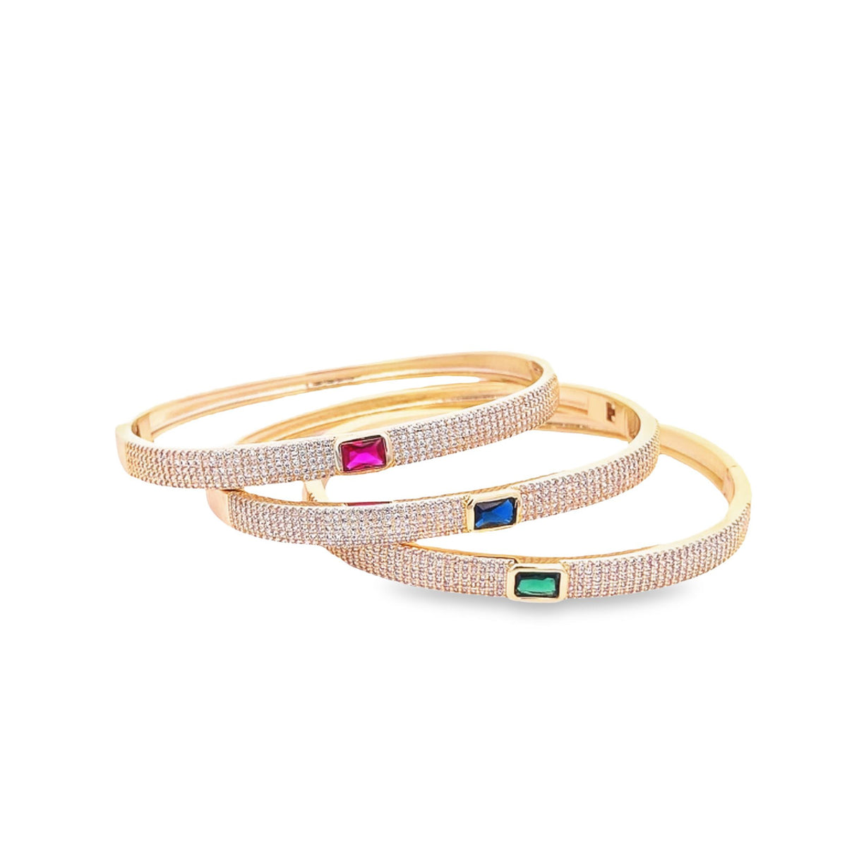 Three pavé-set diamond gold bangles showcase colorful emerald-cut ruby, sapphire, and emerald gemstones against a clean white background.