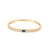 A gold bangle bracelet features a pavé-set crystal band accented with a central rectangular blue sapphire gemstone.