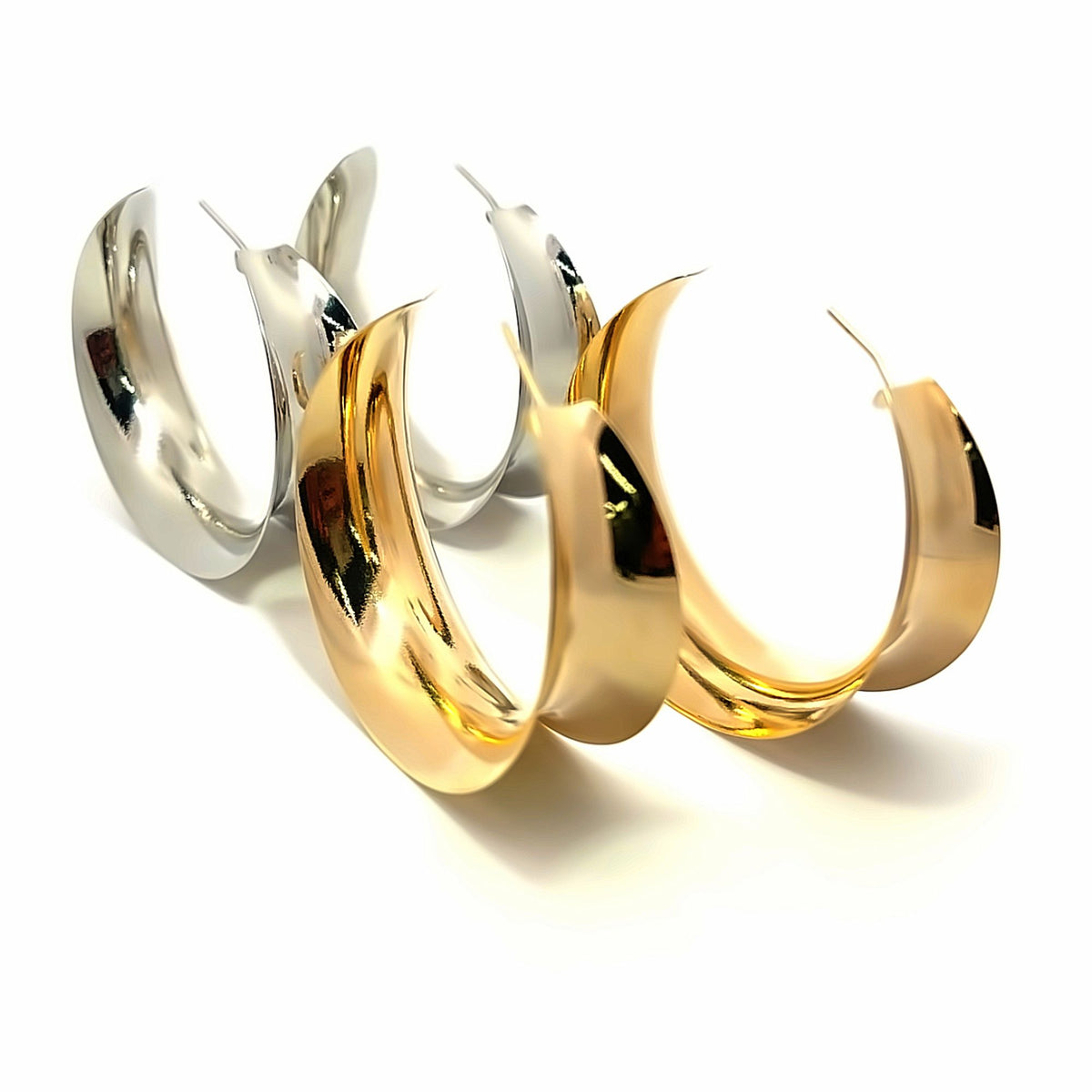 Two pairs of chunky, polished gold and silver hoop earrings display a modern crescent shape against a clean white background.