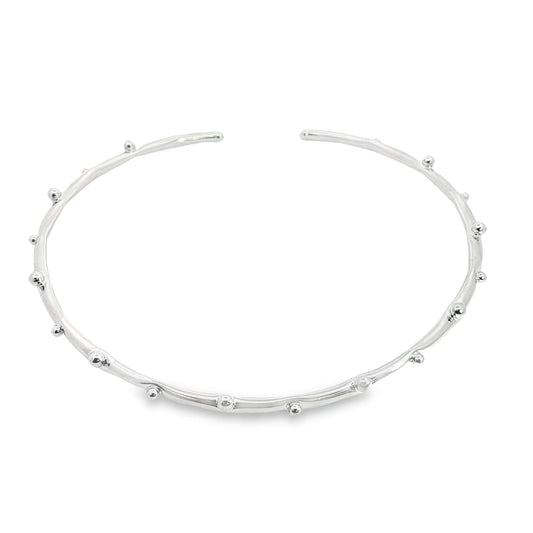 An open silver cuff bracelet featuring delicate bead details rests against a white background.