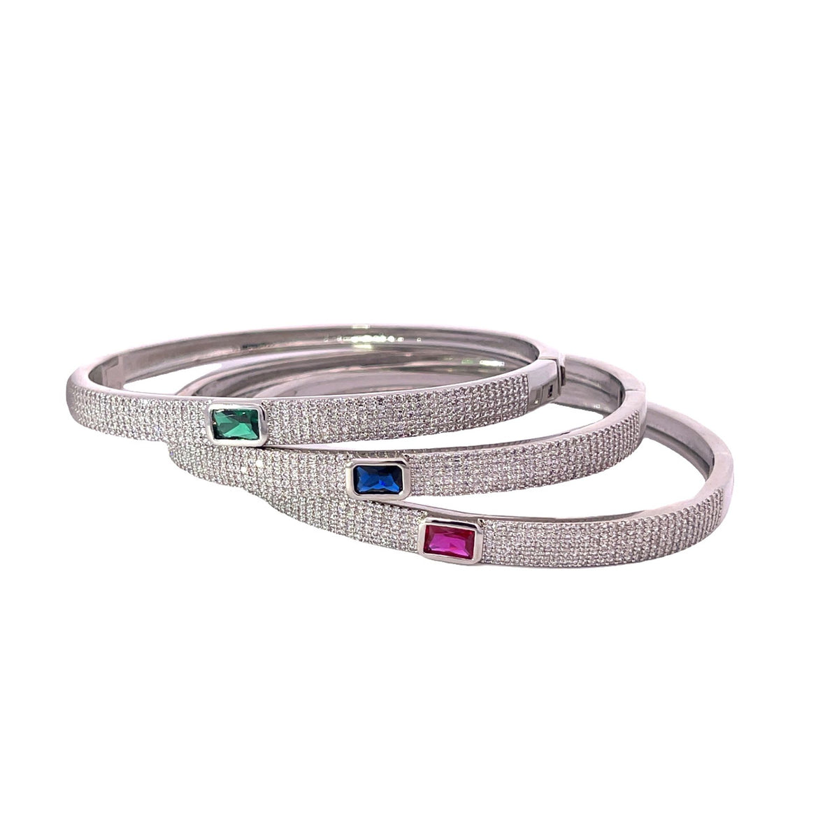 Three pavé-set diamond silver bangles showcase vibrant emerald, sapphire, and ruby baguette gemstones.