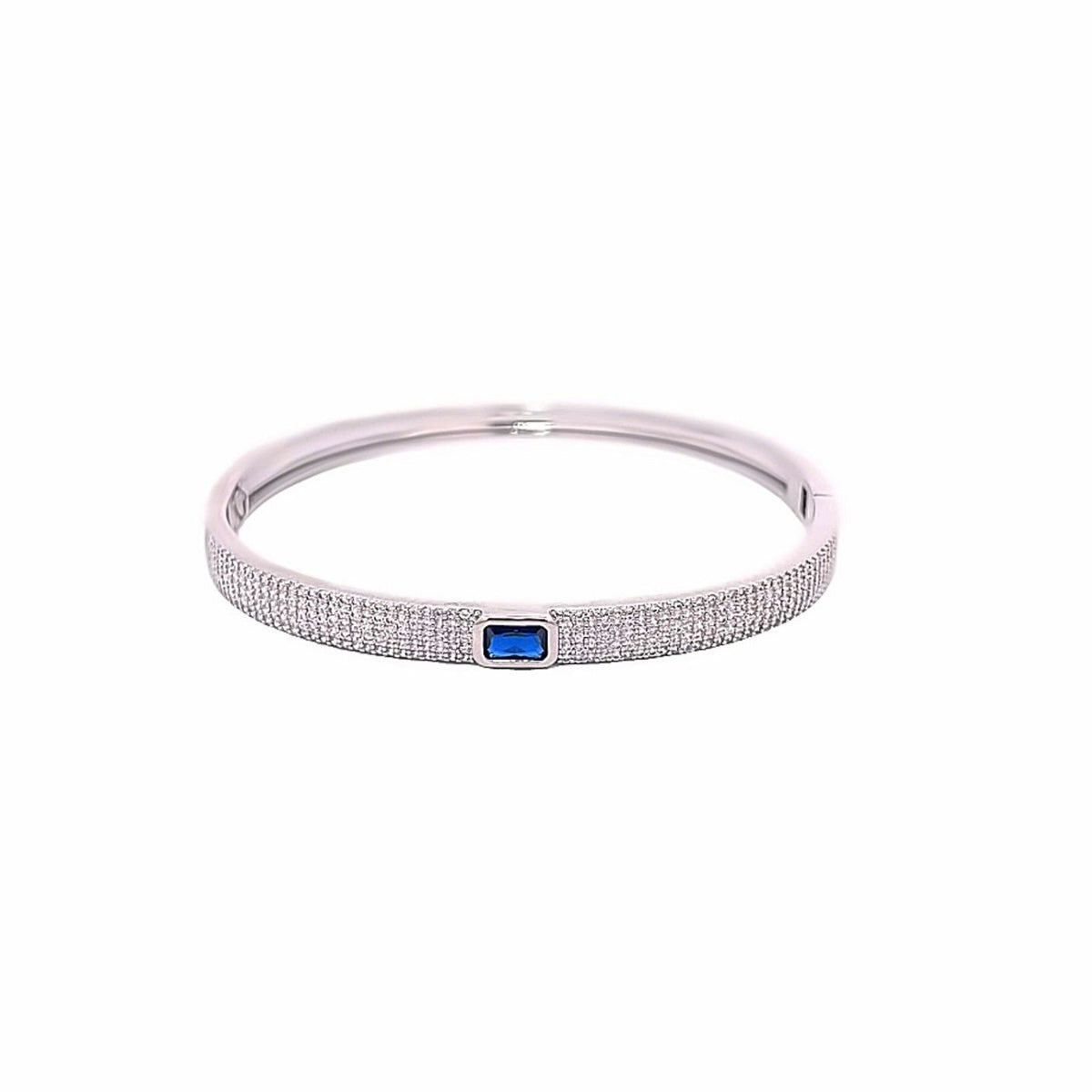 A gleaming silver bangle bracelet showcases a central emerald-cut blue sapphire accented by sparkling pavé diamonds on a clean white background.