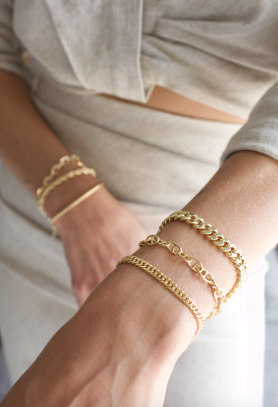 A woman wears a stylish stack of layered gold chain bracelets on her wrist.