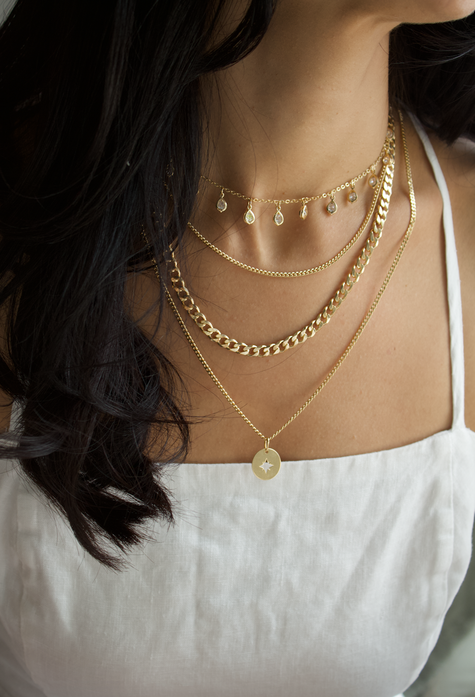 A woman wears a layered set of gold necklaces featuring various delicate chains and a star pendant.