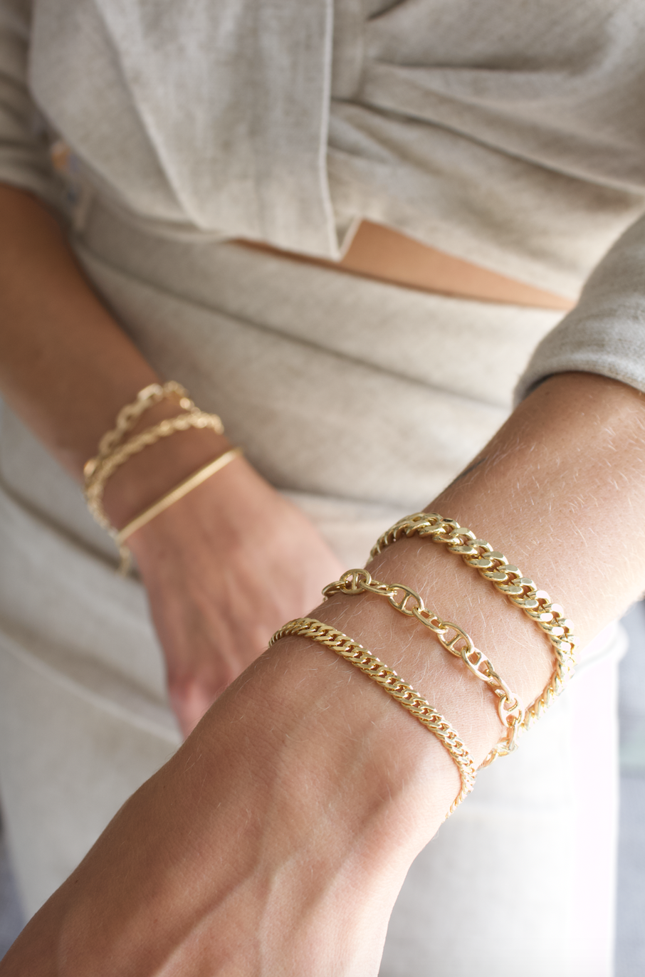 A woman wears a stylish stack of assorted gold chain link bracelets on her wrists.