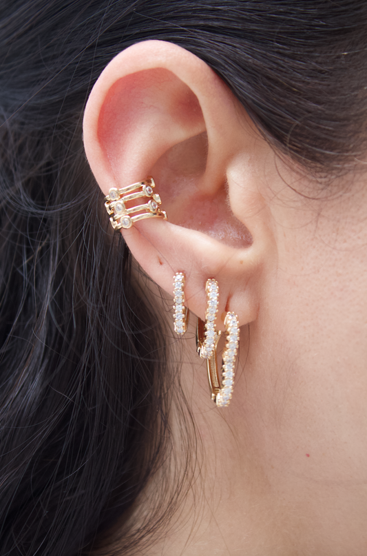 A person wears a set of sparkling gold earrings featuring pavé huggie hoops and a matching ear cuff.