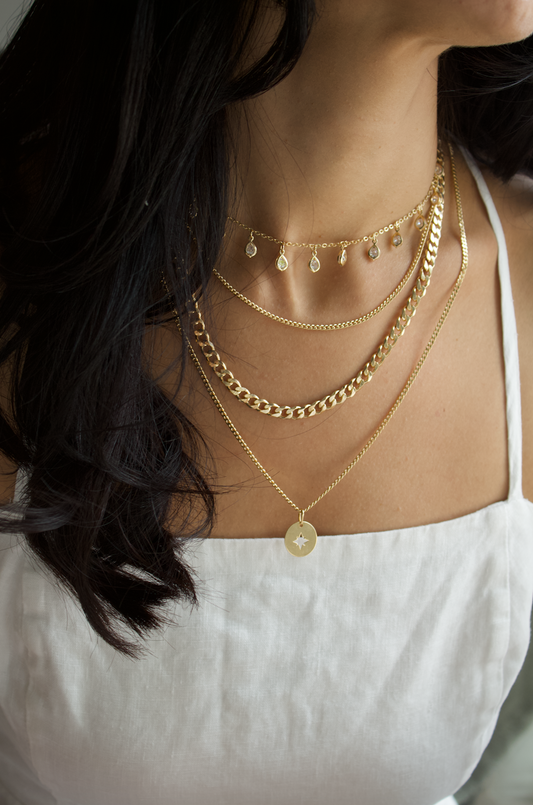 A woman wearing a layered gold necklace set with various chains and pendants.