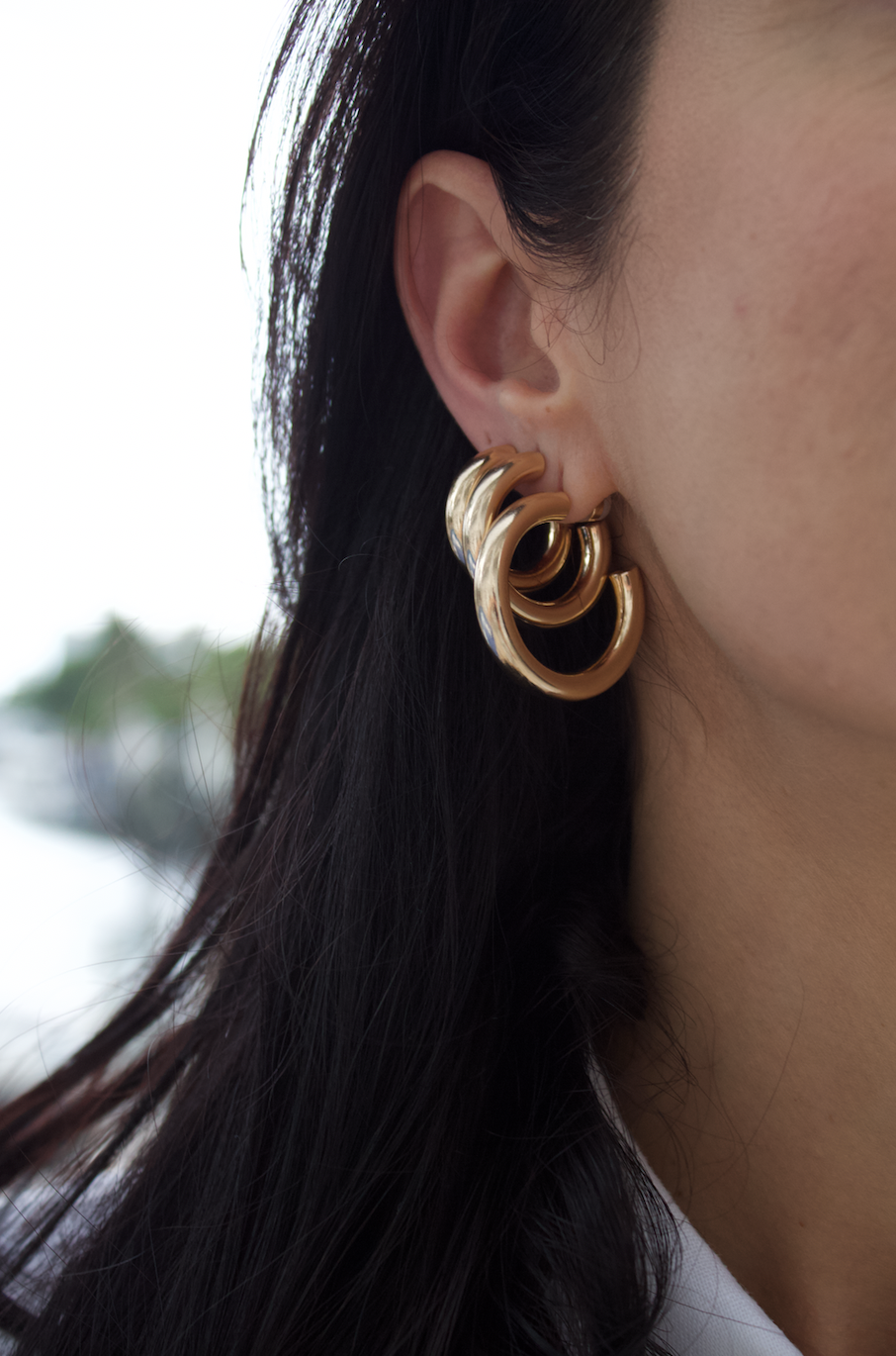 A woman showcases layered chunky gold hoop earrings stacked neatly in her earlobe.
