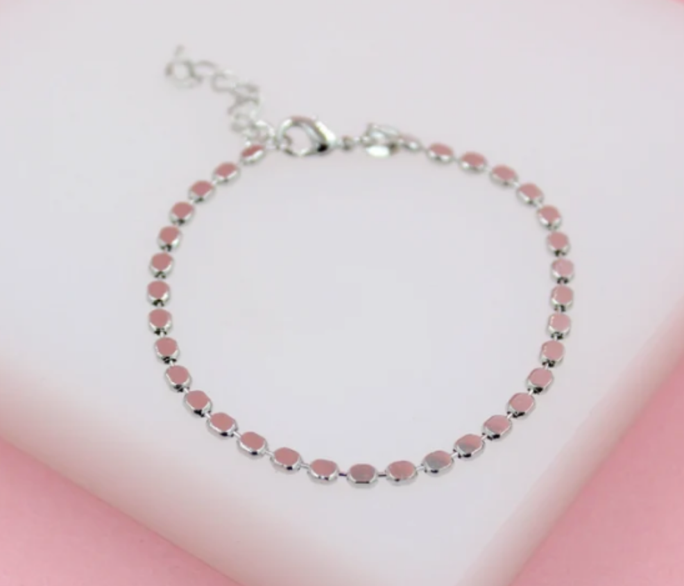 A delicate silver-tone bracelet featuring glossy pink square stations rests on a light pink surface.