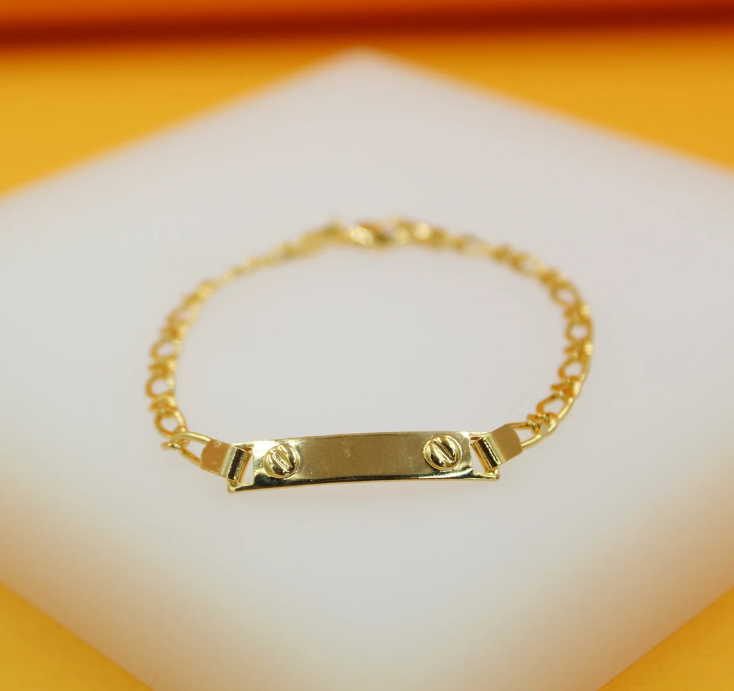 A gold-plated ID bracelet featuring a rectangular plaque accented with two screwhead details rests on a white display surface.