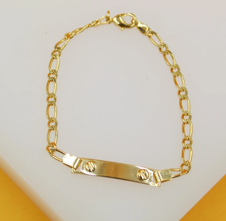 A delicate gold ID bracelet rests on a white display surface, featuring a blank rectangular plate with screw-head details and a classic Figaro chain.