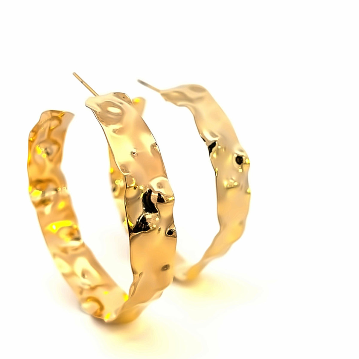 A pair of thick, hammered gold hoop earrings display an organic, textured finish against a plain white background.