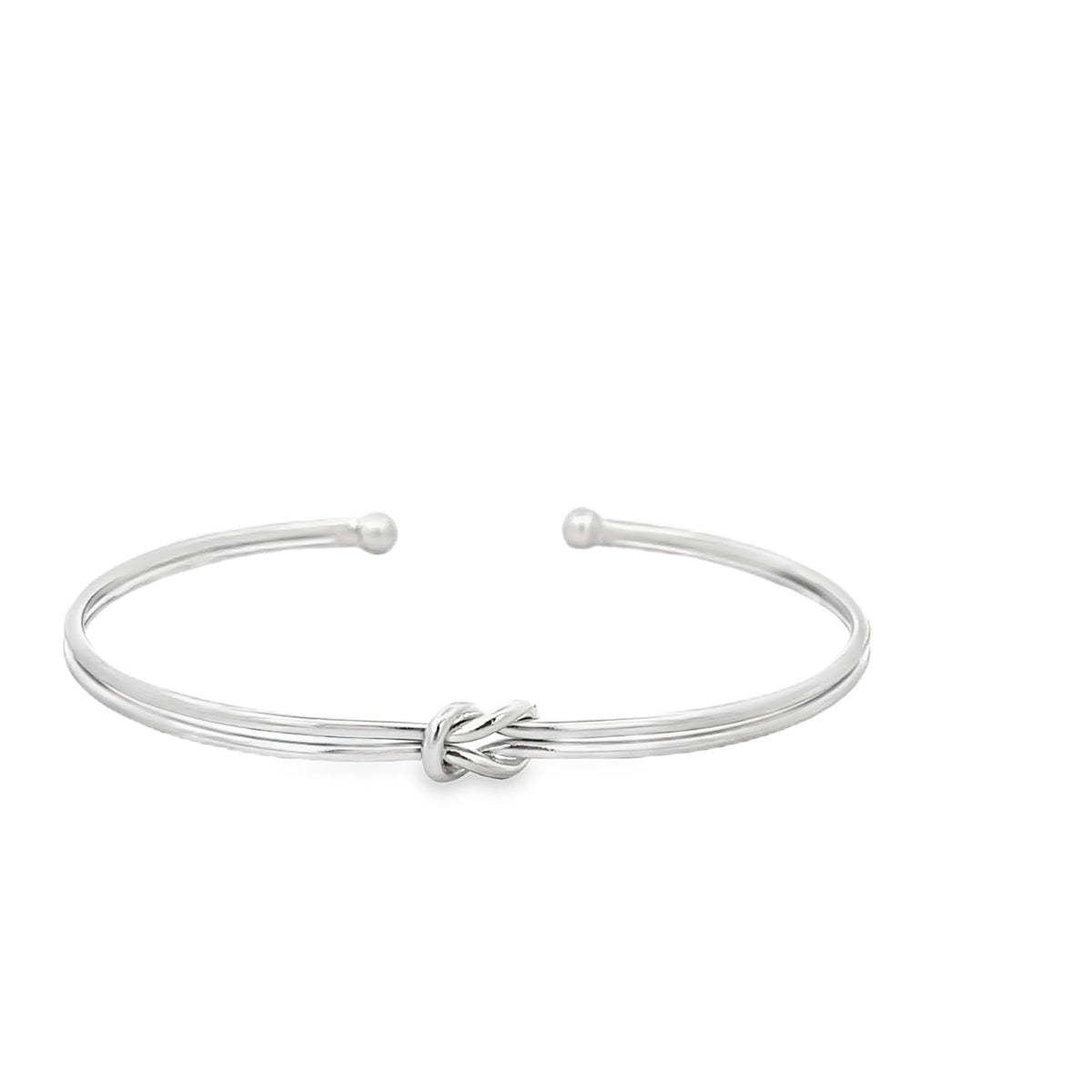 A sleek silver cuff bracelet features a delicate central love knot detail and rounded terminal ends against a clean white background.
