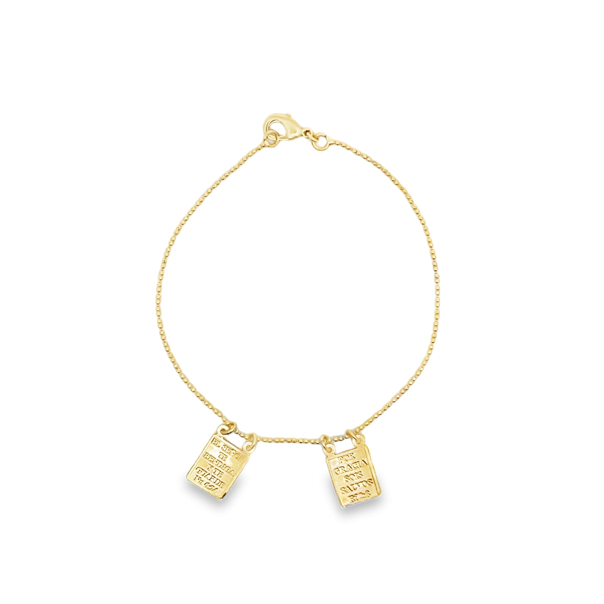A delicate gold chain bracelet features two rectangular engraved religious pendants hanging from the clasp.