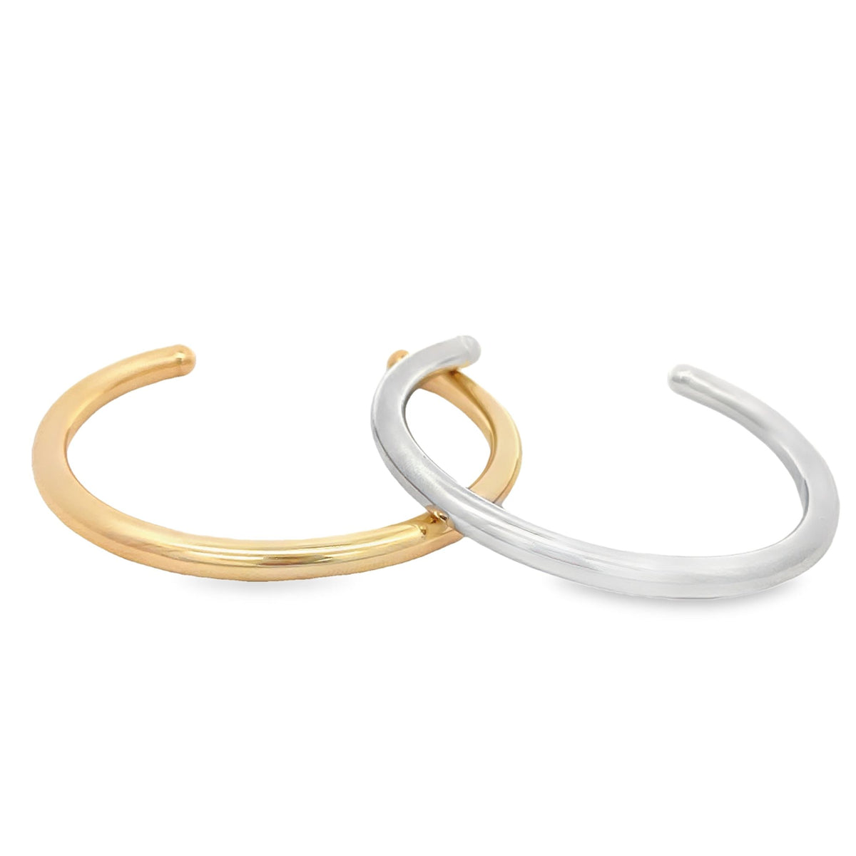A sleek gold cuff bracelet interlocks with a polished silver cuff bracelet against a white background.