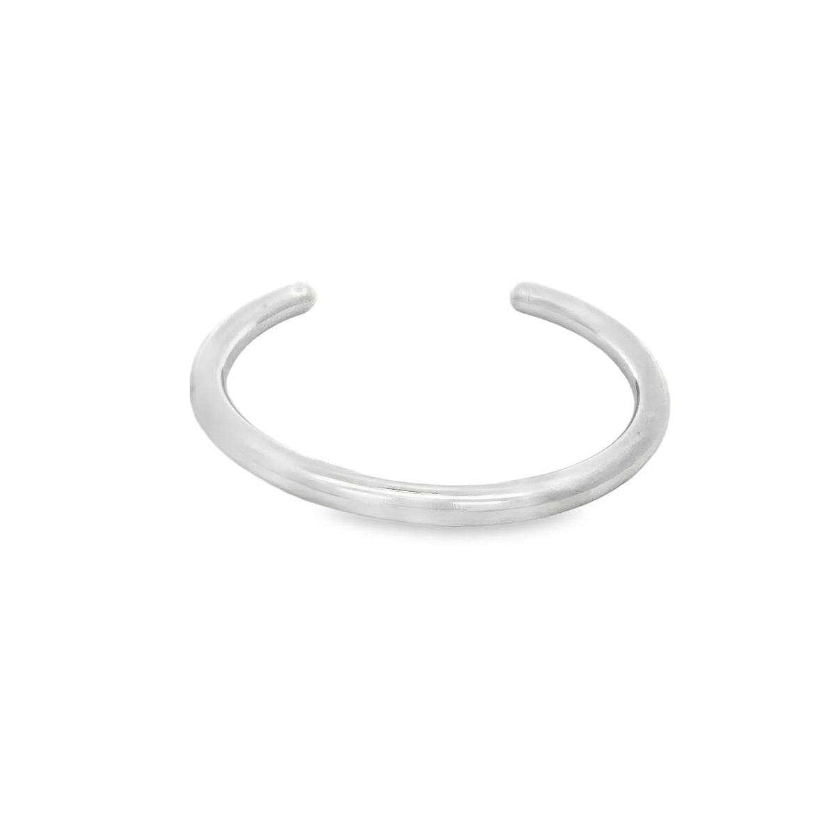 A minimalist silver cuff bracelet rests on a clean white surface, showcasing its sleek open-ended design.