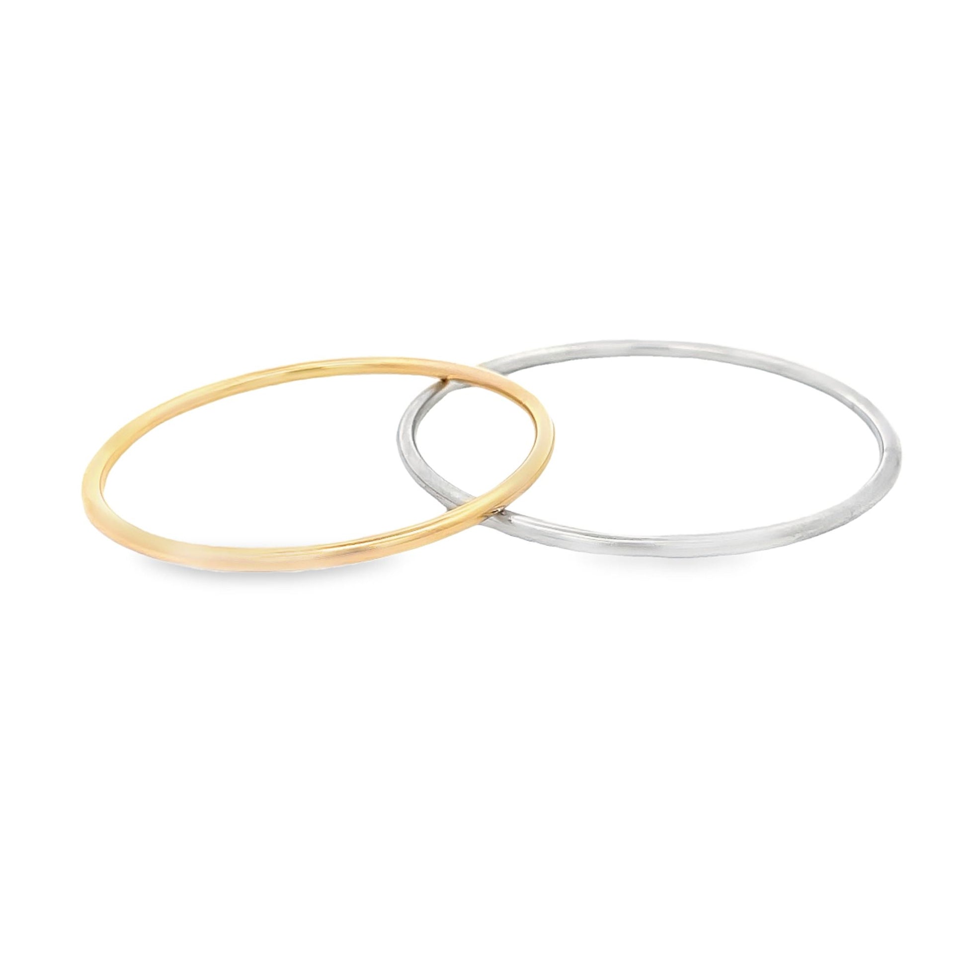 A minimalist yellow gold ring and a sterling silver stacking ring rest intertwined on a clean white background.