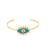 A gold cuff bracelet features a vibrant blue and white enamel evil eye charm with sunburst rays.