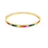 A gold bangle bracelet sparkles with a continuous channel of vibrant, multi-colored baguette-cut gemstones against a clean white background.