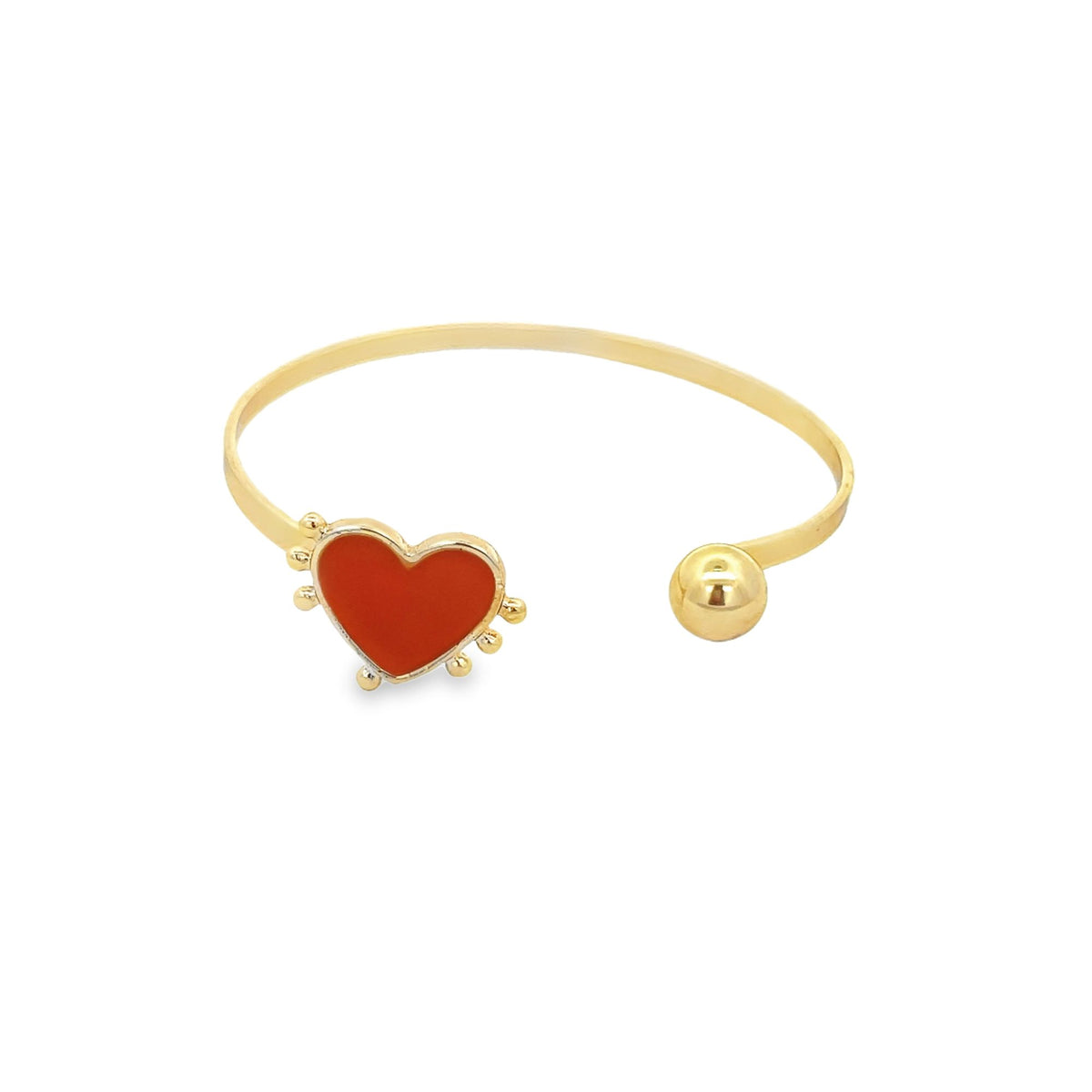 A gold open-cuff bracelet features a vibrant red enamel heart charm on one end and a polished gold sphere on the other.