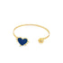 A sleek gold cuff bracelet features a blue enamel heart charm at one end and a polished gold sphere at the other.