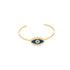 A gold cuff bracelet features a blue and white enamel evil eye charm centered against a white background.