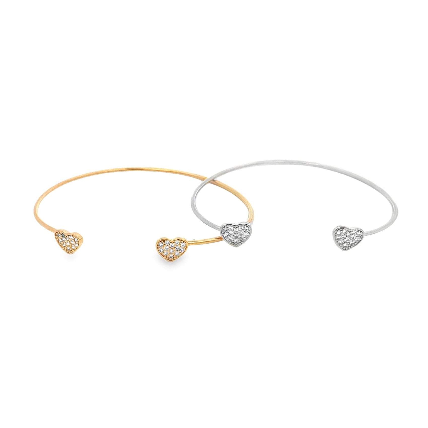 Two delicate cuff bracelets featuring pavé diamond heart charms rest side by side against a white background, with one in yellow gold and the other in silver.