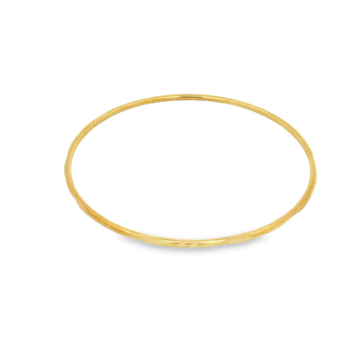 A minimalist gold bangle bracelet rests on a clean white background.