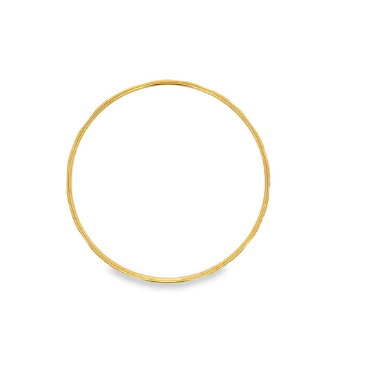 A minimalist gold bangle bracelet rests on a clean white background.