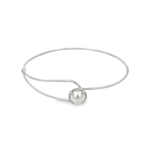 A sleek silver bangle bracelet features a single lustrous white pearl centered in a delicate prong setting.