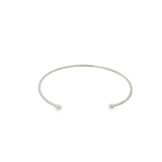 A sleek silver cuff bracelet rests against a plain white background, featuring polished ball ends on each open terminal.