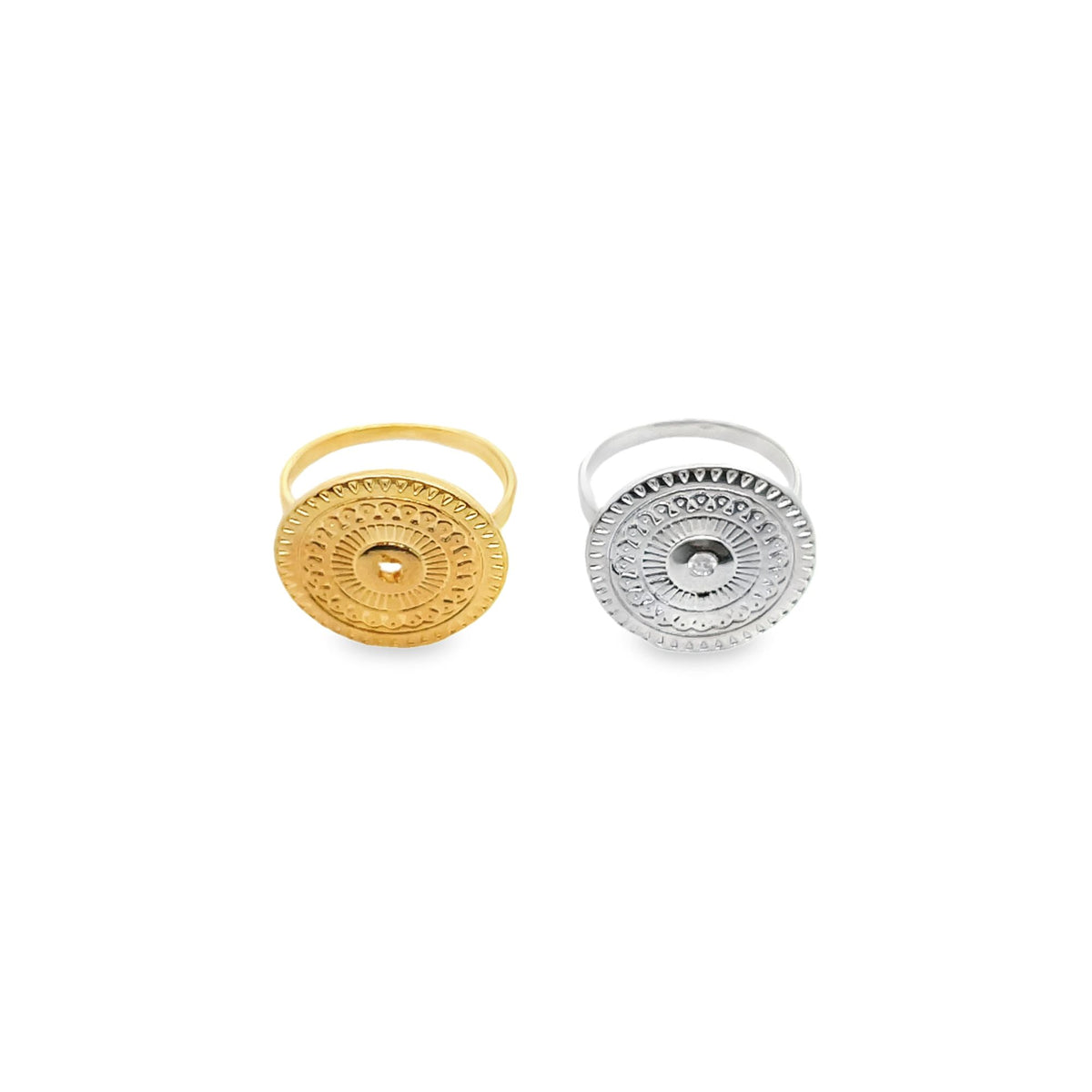 Two statement rings featuring ornate, round medallions lie side by side on a white background, with one crafted in polished gold and the other in gleaming silver.