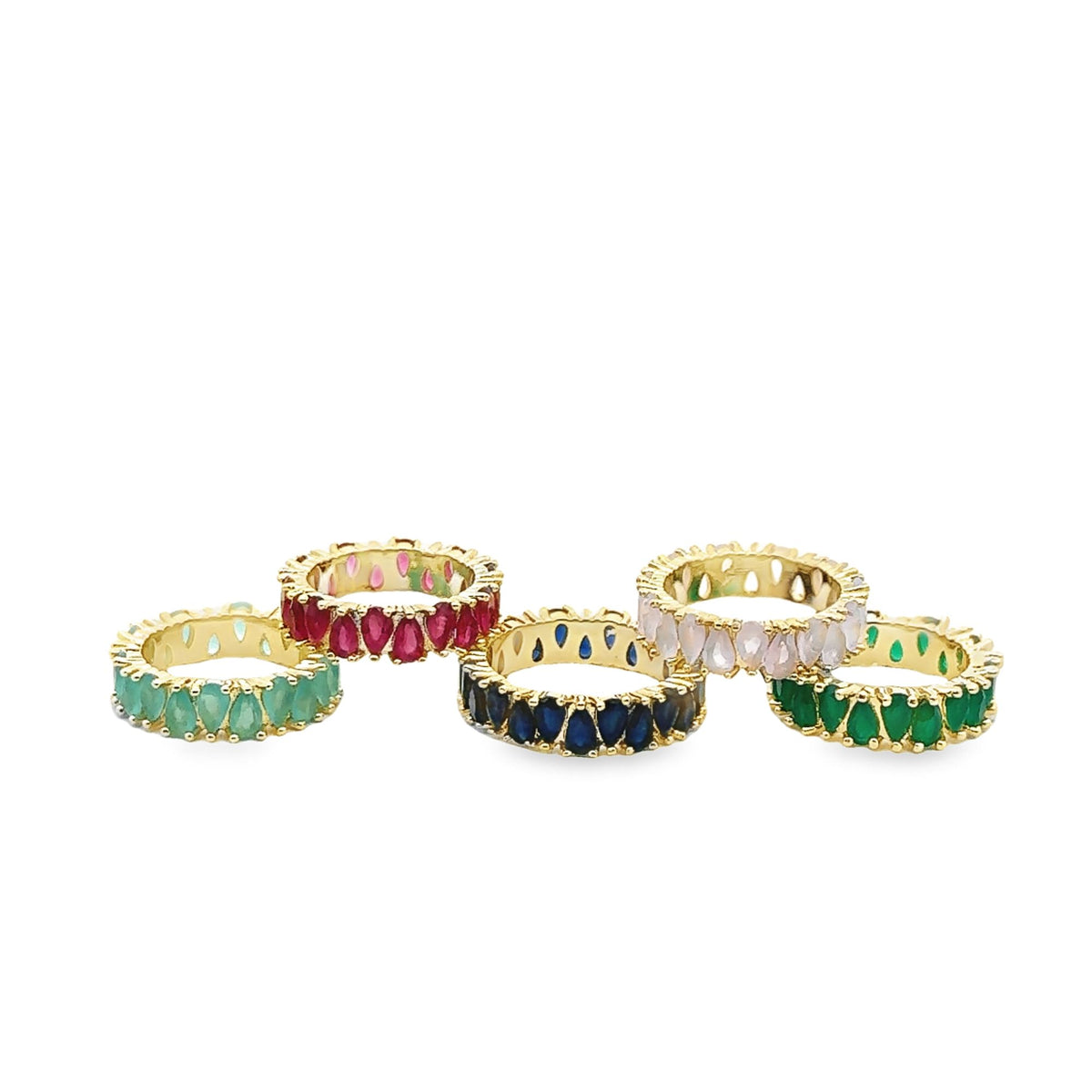 Five gold eternity bands display colorful pear-cut gemstones in red, blue, pink, and varying shades of green against a white background.