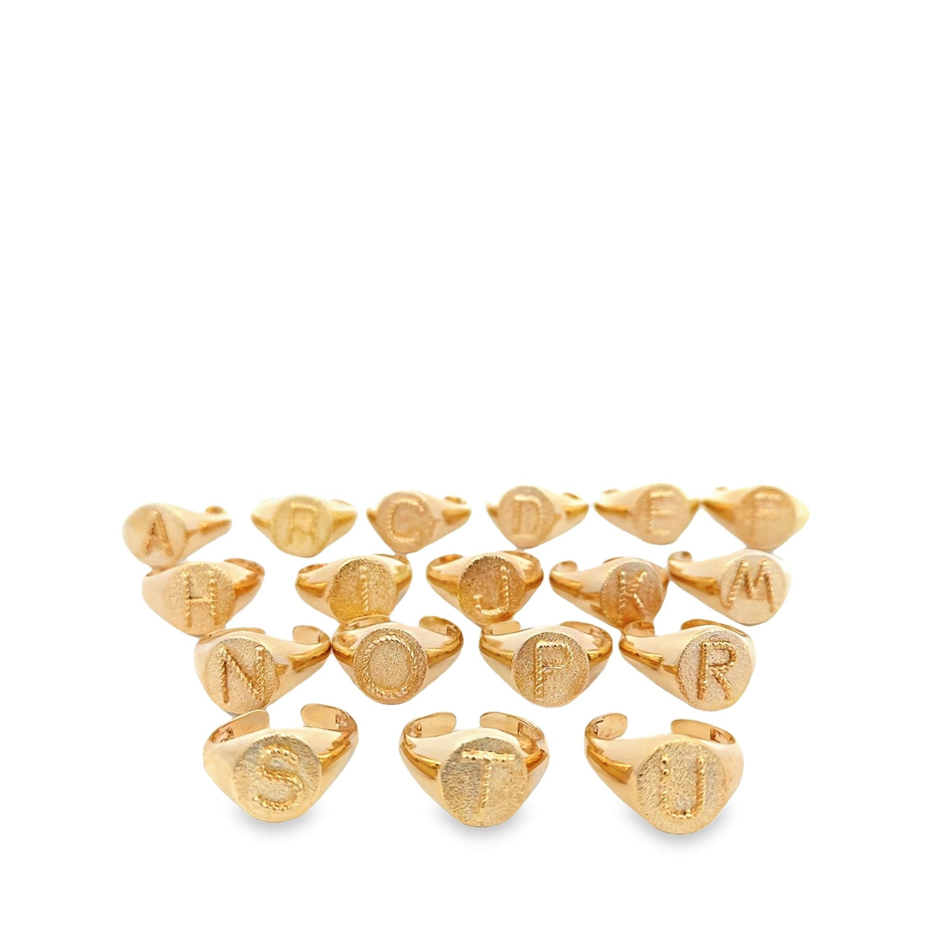 A collection of gold initial signet rings is neatly arranged in rows against a clean white background, showcasing personalized alphabet jewelry.