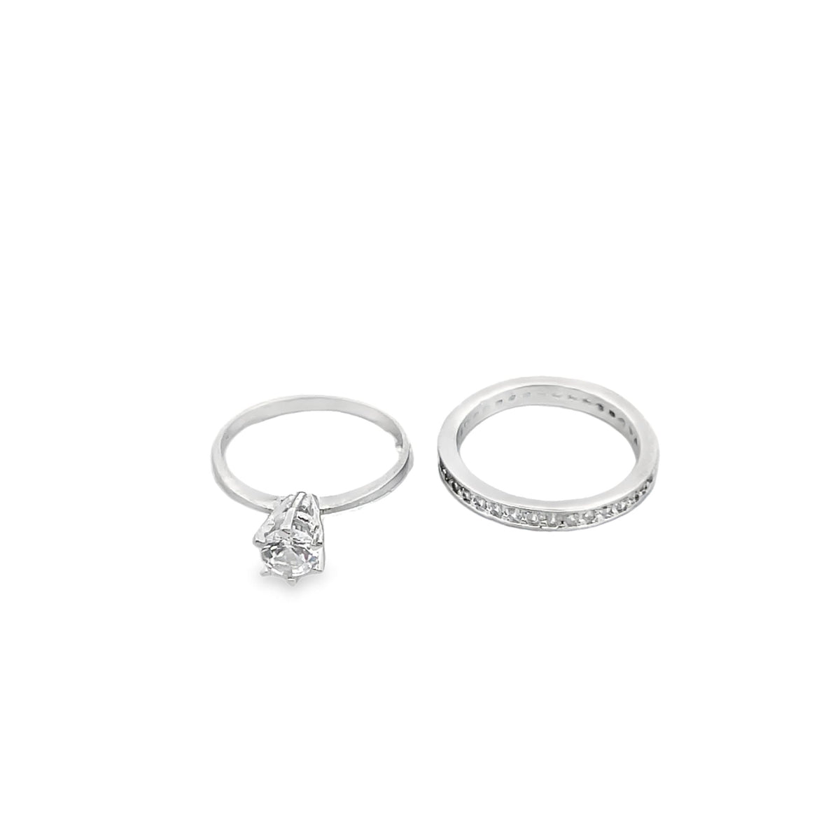 A sparkling silver engagement ring rests beside a matching diamond eternity band against a clean white background.